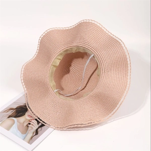 Detail of pink straw sun hat with wavy brim, white lace trim and adjustable wind rope