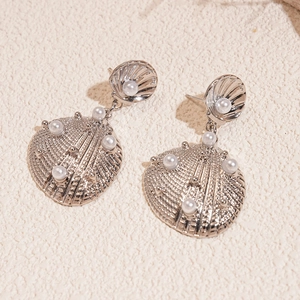 Close-up of silver shell-shaped earrings with textured metal finish and pearls