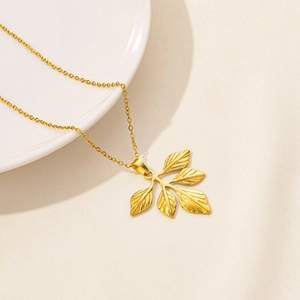 Macro shot of 18K gold ginkgo leaf pendant with detailed texture on white porcelain