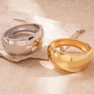 Polished gold and silver irregular wide cuffs displayed on natural textured stone slabs