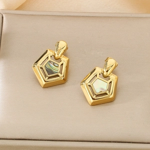 Detailed shot of golden pentagonal shell earrings on beige jewelry box lining