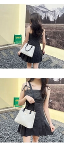 Detail view of a white minimalist leather handbag with black handles and shoulder strap