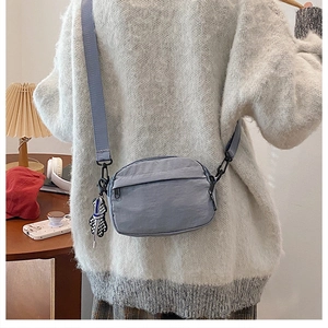 Gros plan d'un sac bandoulière en nylon bleu clair avec un ours à carreaux sur un pull blanc