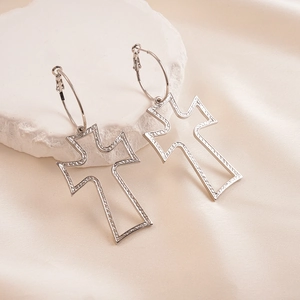 Close-up of silver hollow cross earrings with engraved textures on a stone plate