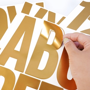 Detail of 5-inch shiny gold letter sticker being peeled from the backing sheet