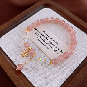 Détail d'un bracelet en cristal de fraise perlé avec un pendentif fleur de cerisier doré