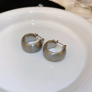 Close-up of matte brushed silver geometric hoop earrings on a white ceramic plate
