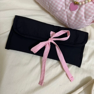 Vue détaillée d'une trousse en tissu noir avec un nœud en ruban rose et fermeture enveloppe