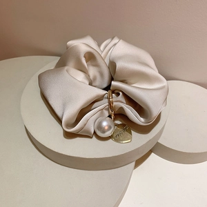 Detail of beige satin scrunchie with faux pearl and engraved heart charm on tiered stands