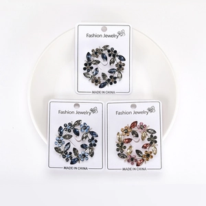 Detailed view of three crystal wreath brooches in blue and brown on a white display tray