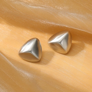 Macro shot of matte silver triangular stud earrings on champagne silk fabric background