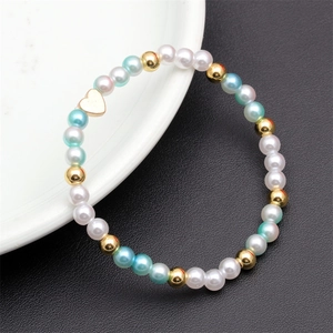 Detail of beaded bracelet with blue and white pearls, golden heart charm, and metal beads