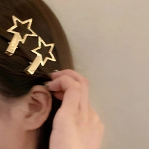 Detail of two gold metal star-shaped hair claws worn on hair for a Y2K aesthetic look