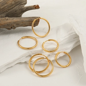 Three pairs of different sized gold titanium steel hoop earrings on white stone slabs