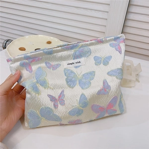 Detail of cream jacquard makeup bag with blue and pink butterfly embroidery and text label