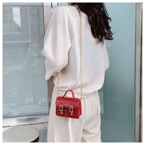 Detail of red patent leather mini crossbody bag with elegant gold chain strap and glossy finish