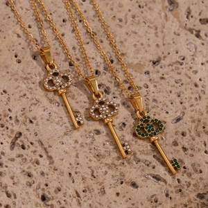 Detail view of gold key pendants with zircon, pearl, and green stone on stone background