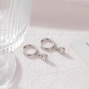 Minimalist silver drop earrings with pear-cut zircon pendants on a pink textured background