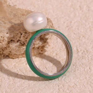 Macro detail of silver stainless steel ring with green enamel and a white pearl