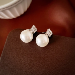 Macro detail of elegant pearl earrings with zircon inlay on a brown leather surface
