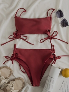 Flat lay of deep red high-waisted bikini with side tie bows and vacation accessories