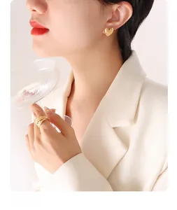 Close-up of golden heart-shaped textured earrings and feather pattern ring on a model