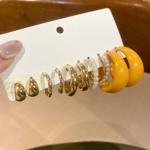 Close-up of acrylic C-shaped earring set with gold hoops and pearls on display card
