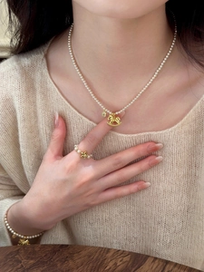 Close-up of pearl bead necklace set with gold trojan horse and coin charms on a model