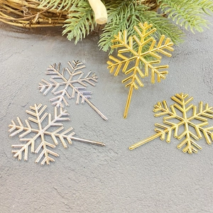 Detail showing four gold and silver snowflake cake toppers on a festive textured surface