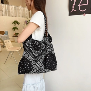 Black and white paisley floral canvas tote bag shown on shoulder in a cozy cafe setting