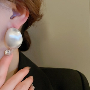 Close-up of oversized white round pearl earring worn by a model in soft lighting
