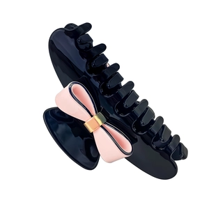 Detail of black glossy hair claw clip featuring a pink 3D bow with golden metal buckle