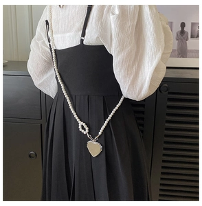 Close-up of pearl crossbody chain featuring a polished silver heart pendant on a model