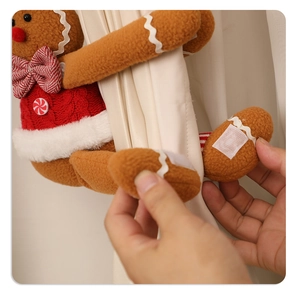 Gingerbread man plush curtain tieback in red sweater shown on a beige curtain