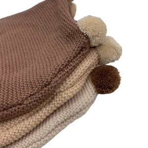 Close-up of knit baby hats with soft pom-poms in coffee, camel, and cream colors
