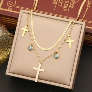 Double-layered gold necklace with crystal cross and turquoise beads in a jewelry box