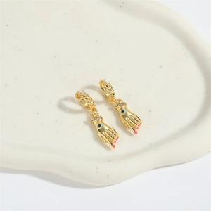 Detailed macro shot of gold palm earrings with evil eye center and pink nail accents