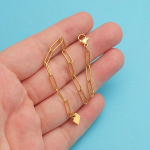 Gold paperclip chain bracelet with a square pendant and lobster clasp on blue background