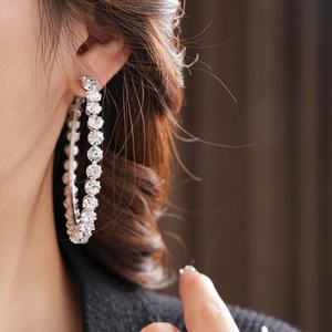 Close-up of a silver hoop earring featuring encrusted clear crystals on a model