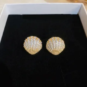 Elegant gold shell earrings with pavé zircons and pearls on black velvet display