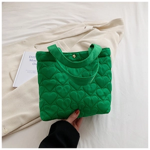 Detail of green heart quilted tote bag with metal buckle near white corduroy jacket