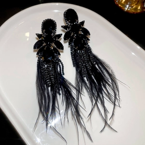 Macro shot of long black feather tassel earrings with crystal settings on white tray