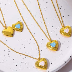 Golden heart locket necklace with blue and white opal stones on white ceramic tray