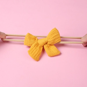 Detail view of stretching yellow muslin bow headband showing soft elastic nylon band