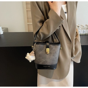 Détail du sac seau bicolore avec fermoir doré et charme en peluche sur un blazer