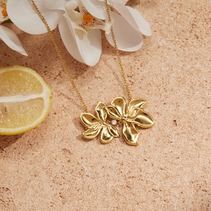 Elegant gold flower pendant necklace with central diamond on a summer-themed stone surface