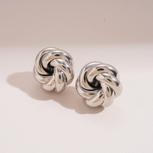 Detail of silver metallic knot stud earrings with a glossy swirl floral design
