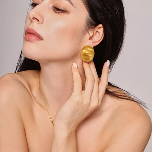 Golden large round textured earrings with wavy design shown on female model