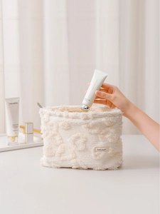 Creamy white plush heart makeup bag with textured surface being filled with hand cream