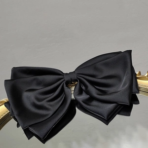 Close-up of elegant black satin bow hair clip on a decorative gold mirrored tray